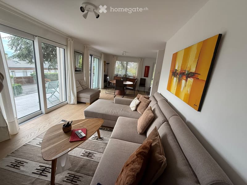 Modern living room with a large sectional sofa, coffee table, dining area with chairs and table, large windows with curtains, and artwork on the wall.