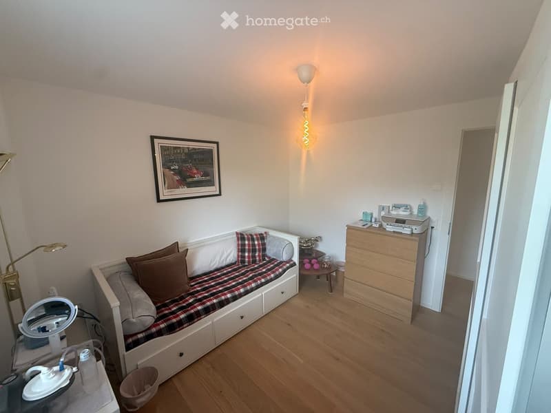 Cozy, compact bedroom with a sofa bed, small table, lamp, mirror, and printer on a wooden floor.