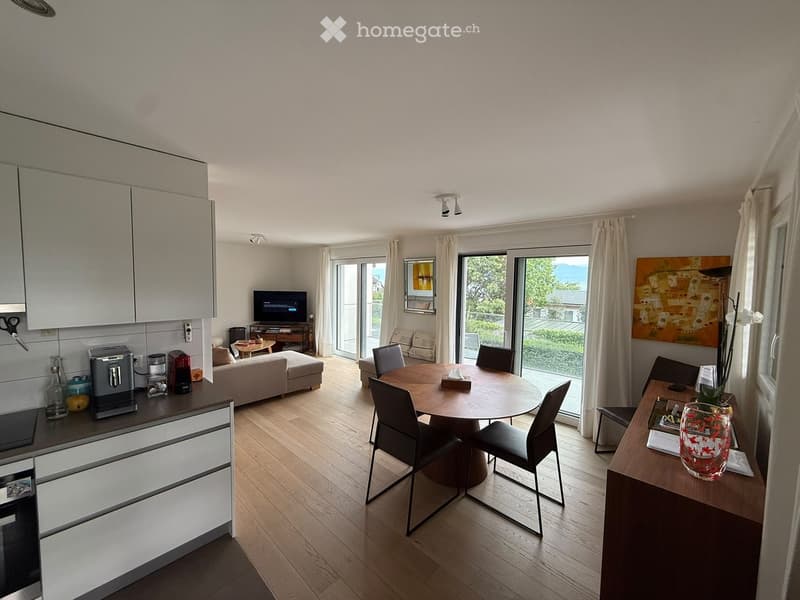 Open-plan living and dining area with modern furniture, including a sofa, coffee table, dining table with chairs, and a kitchen area with cabinets and appliances.
