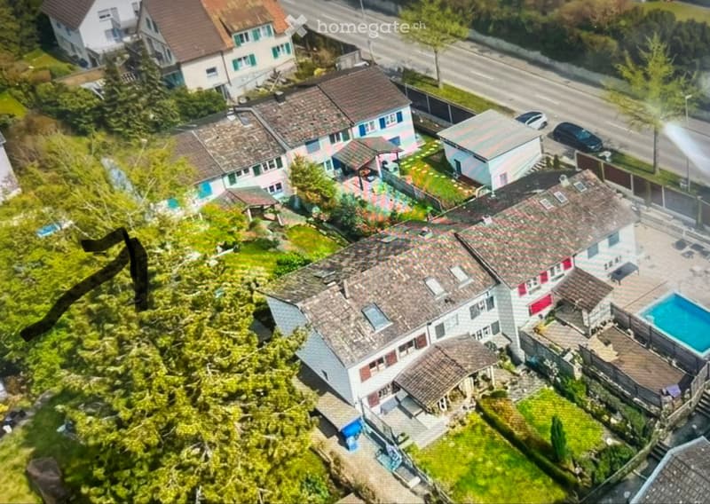 Aerial view of a residential area with multiple houses, gardens, and a swimming pool in the foreground.