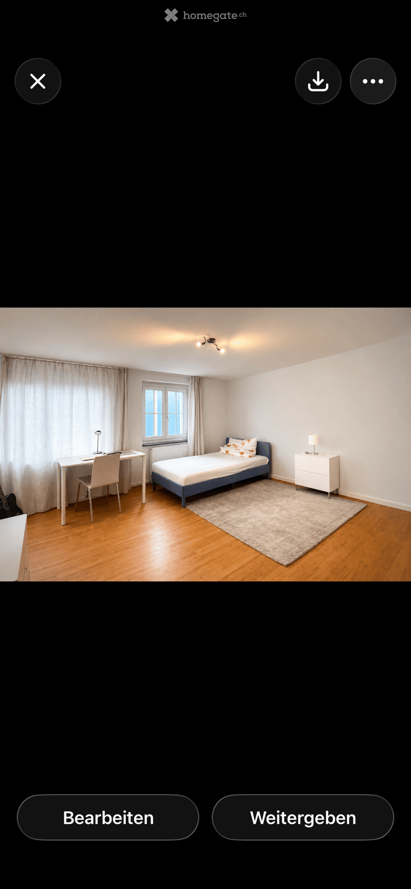 A well-lit bedroom with a single bed, desk, chair, nightstand, and guitar. The room features wooden flooring, white walls, and a window with curtains.