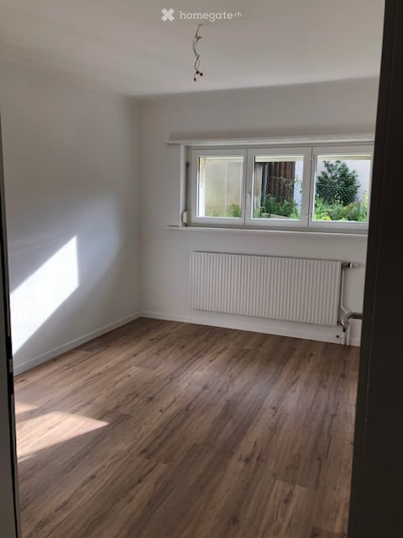 Empty room with wooden flooring, white walls, and a radiator under a large window with three panes.