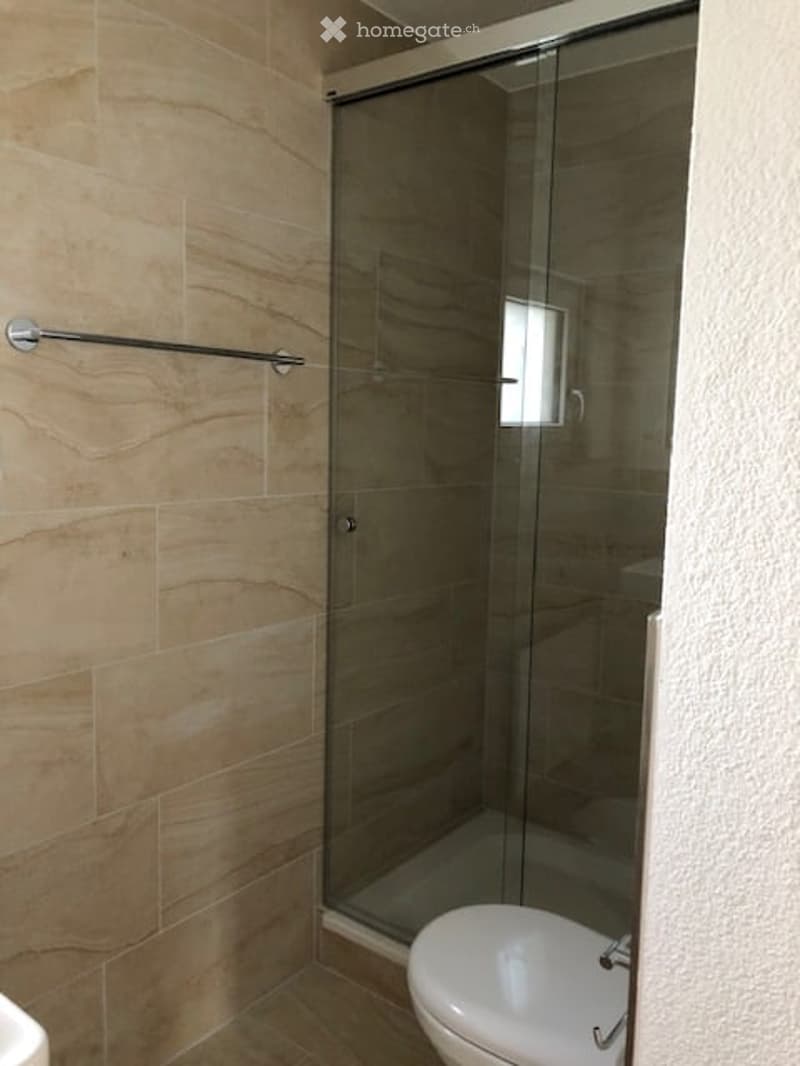 Modern bathroom with beige tiled walls, a white toilet, and a glass shower enclosure.