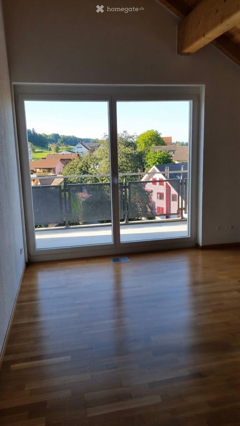 Empty room with wooden flooring and large sliding glass doors leading to a balcony with a scenic view of the surrounding area.