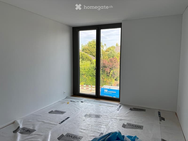 Empty room with white walls, large sliding glass doors, and protective floor covering.
