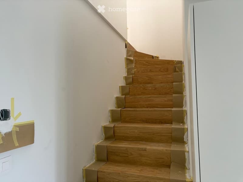 Wooden staircase with beige carpeting, white walls, and a small light fixture on the left side.