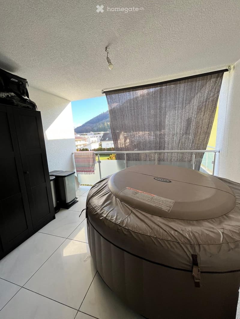 Balcony with a covered hot tub, glass railing, and scenic mountain view.
