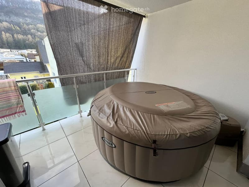 Balcony with a round inflatable hot tub, glass railing, and scenic mountain view.