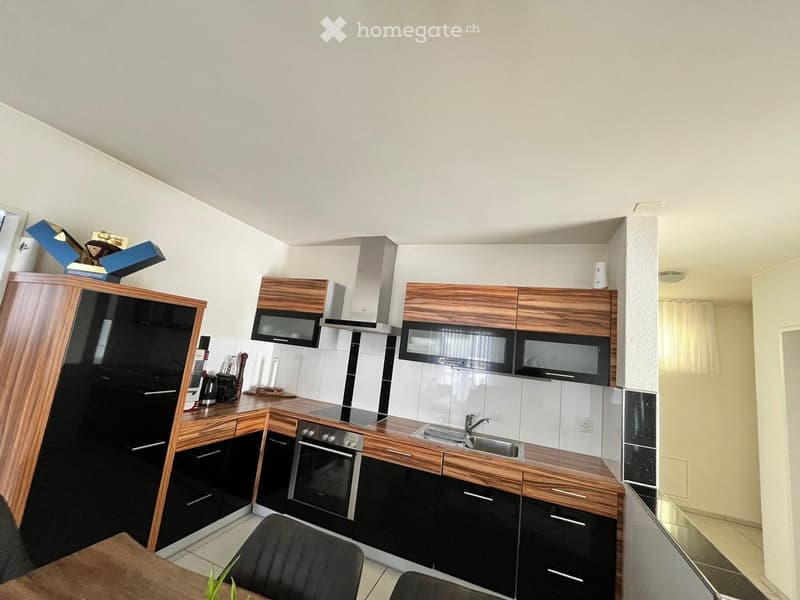 Modern kitchen with wooden and black cabinetry, stainless steel appliances, and a small dining area with a table and chairs.