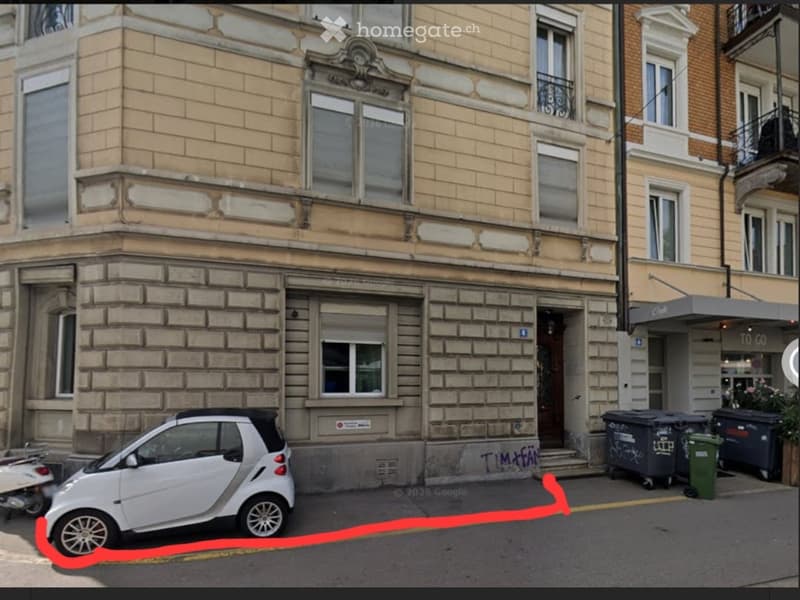 Classic European building with stone facade, multiple windows, and a small parking space for a car in front.