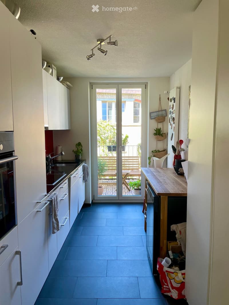 Modern kitchen with white cabinets, stainless steel appliances, and a wooden island. Features a sliding glass door leading to a balcony with outdoor seating.