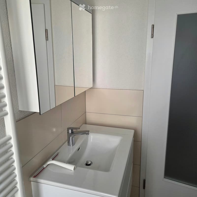Modern bathroom with a white sink, chrome faucet, mirrored cabinet, and beige tiled walls.