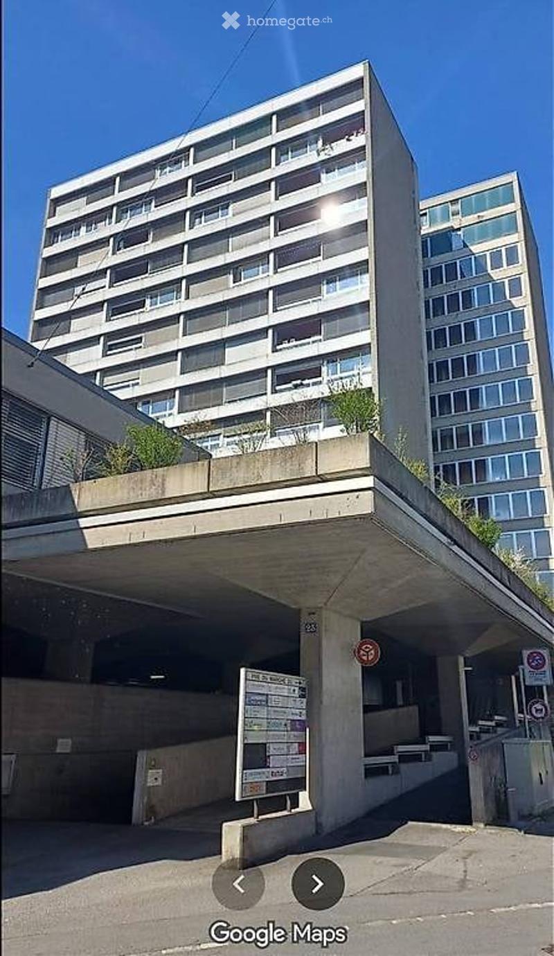 Modern multi-story apartment building with a covered parking area and signage.