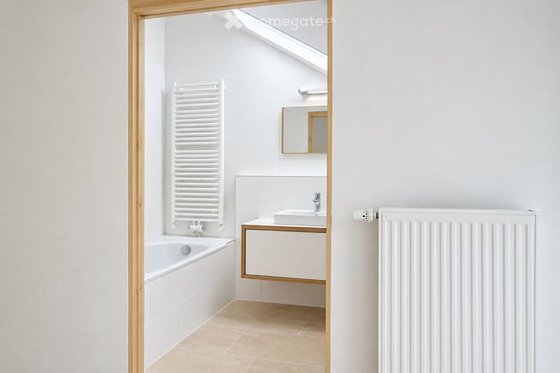 Modern bathroom with white tiles, a bathtub, a sink with a wooden cabinet, a mirror, and radiators on both sides.