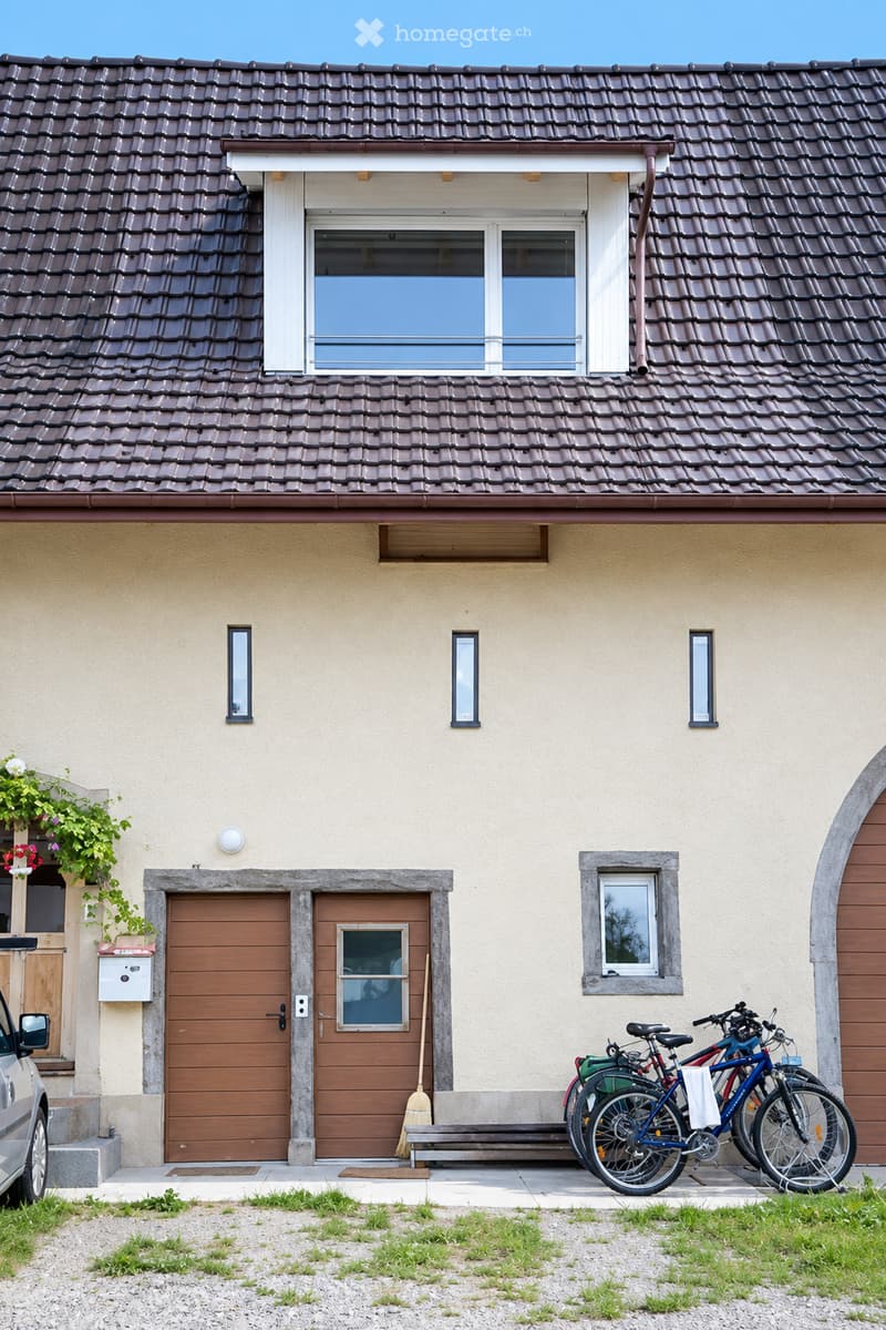 Two-story house with beige walls, brown wooden doors, multiple windows, and bicycles parked outside.