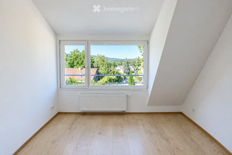 Empty room with wooden flooring, white walls, large window offering a view of greenery and houses, and a radiator below the window.