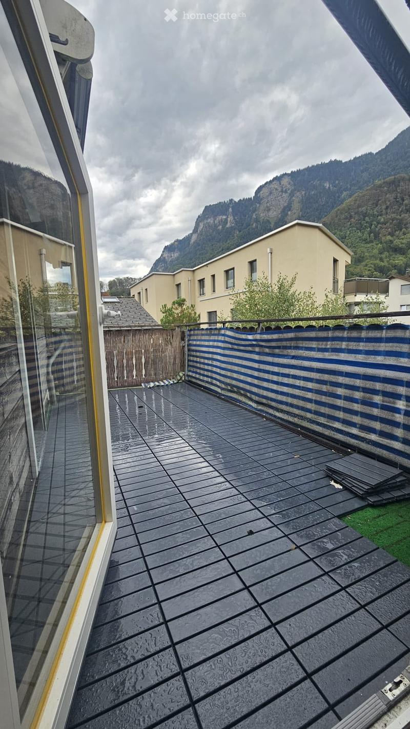 Balcony with dark tiled flooring, wooden fence, and a view of surrounding buildings and mountains.