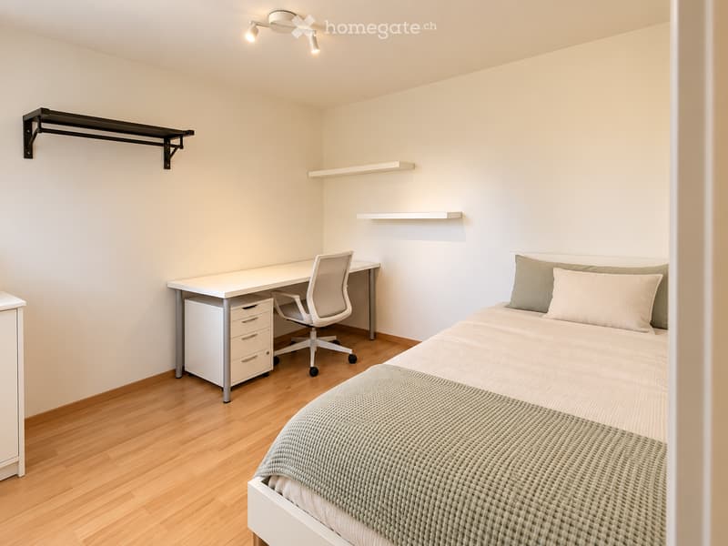 A modern, minimalist bedroom with a single bed, a desk with a chair, and built-in shelves. The room features light-colored walls, wooden flooring, and a sleek, contemporary design.