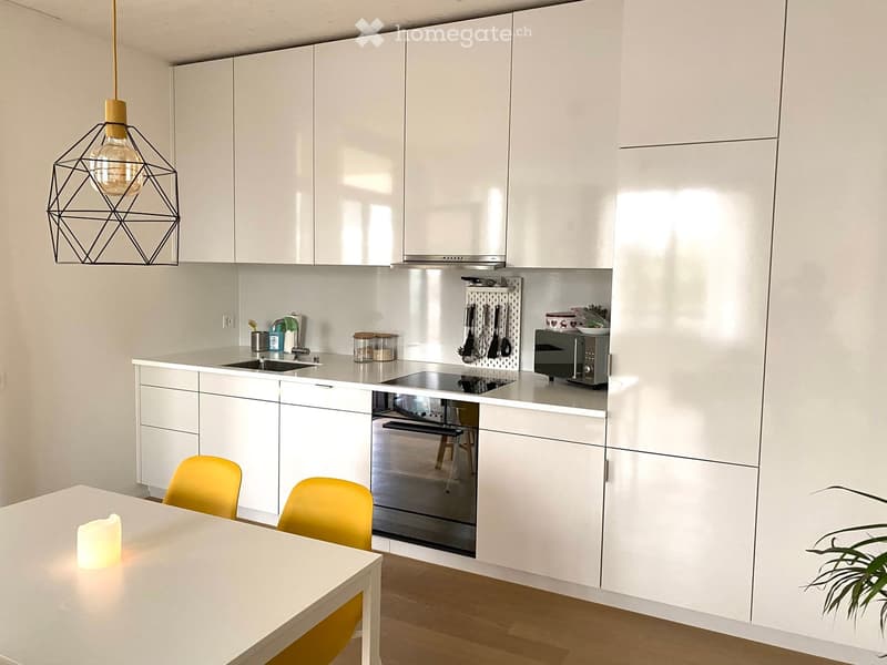 Modern kitchen with white cabinets, stainless steel appliances, a central island, and a dining area with yellow chairs.
