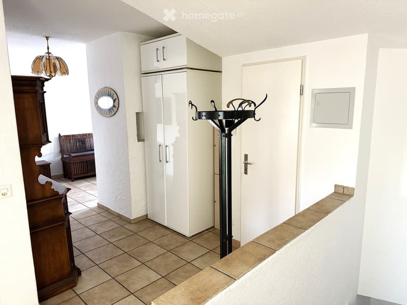 Hallway with tiled floor, white walls, a coat rack, a wooden bench, and a chandelier.