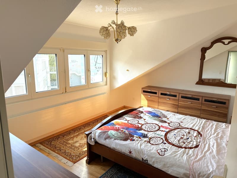 Cozy attic bedroom with wooden bed, colorful quilt, wooden cabinet, mirror, and chandelier.