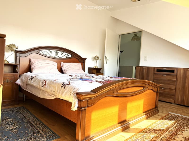 Cozy bedroom with a wooden bed, nightstands, lamps, and a patterned rug on the floor.