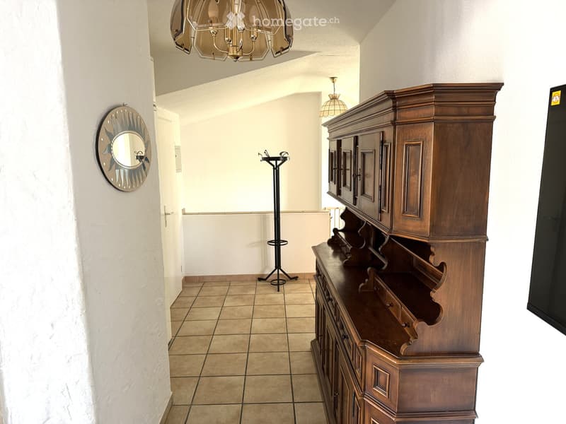 Hallway with tiled floor, white walls, wooden cabinet, coat rack, and decorative mirror on the wall.