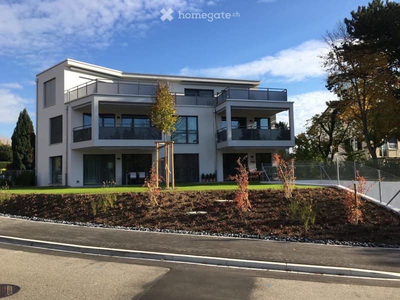 Modern two-story house with large windows, balconies, and a landscaped front yard.
