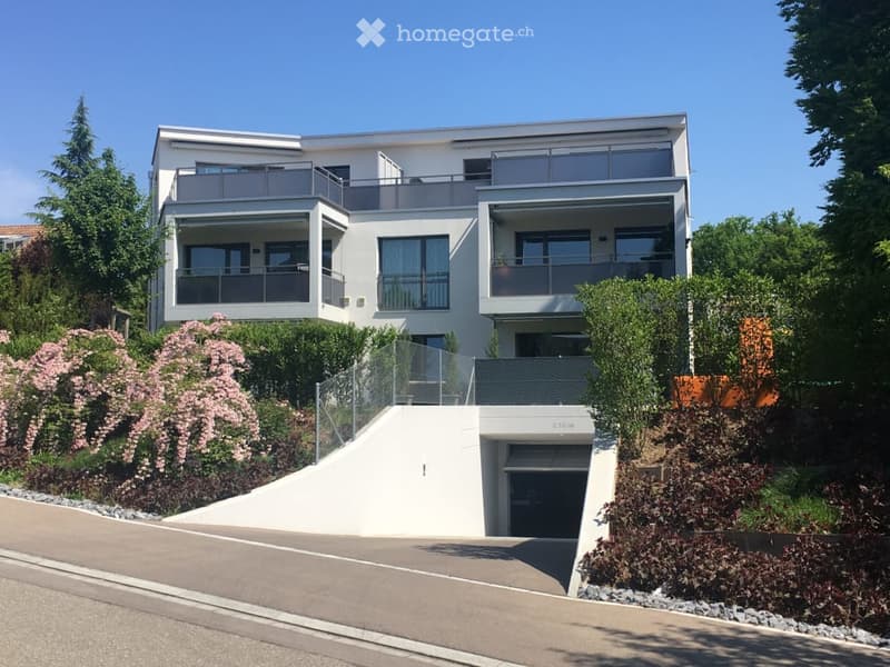 Modern two-story house with white exterior, large windows, multiple balconies, and a garage entrance.