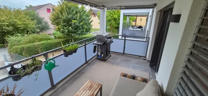 Balcony with a small seating area, a table, a grill, and potted plants.