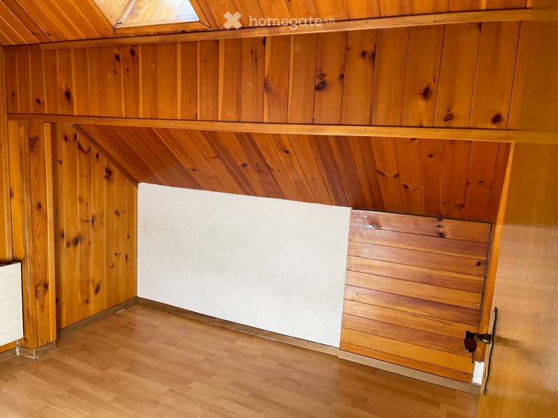 Empty room with wooden walls, ceiling, and floor, featuring a whiteboard on one wall and a partially open door.