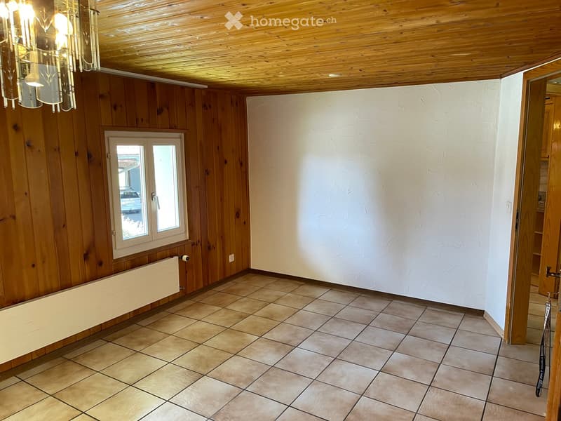 Empty room with wooden walls, tiled floor, and a window with white frame. Wooden ceiling and radiator visible.