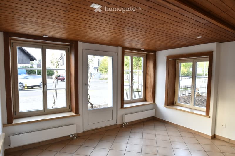 Empty room with tiled floor, white walls, wooden ceiling, and multiple windows with radiators beneath them.
