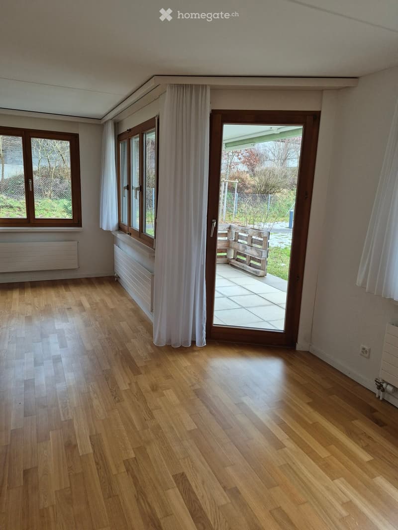 Empty room with wooden flooring, large windows, and a sliding glass door leading to a patio area.
