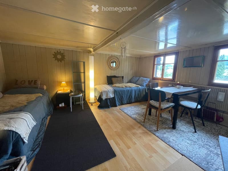 Cozy bedroom with two beds, a small table with chairs, a lamp, and a mirror on the wall.