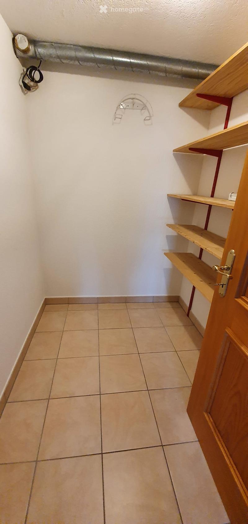 Empty room with tiled floor, white walls, wooden door, and wooden shelves on the right side.