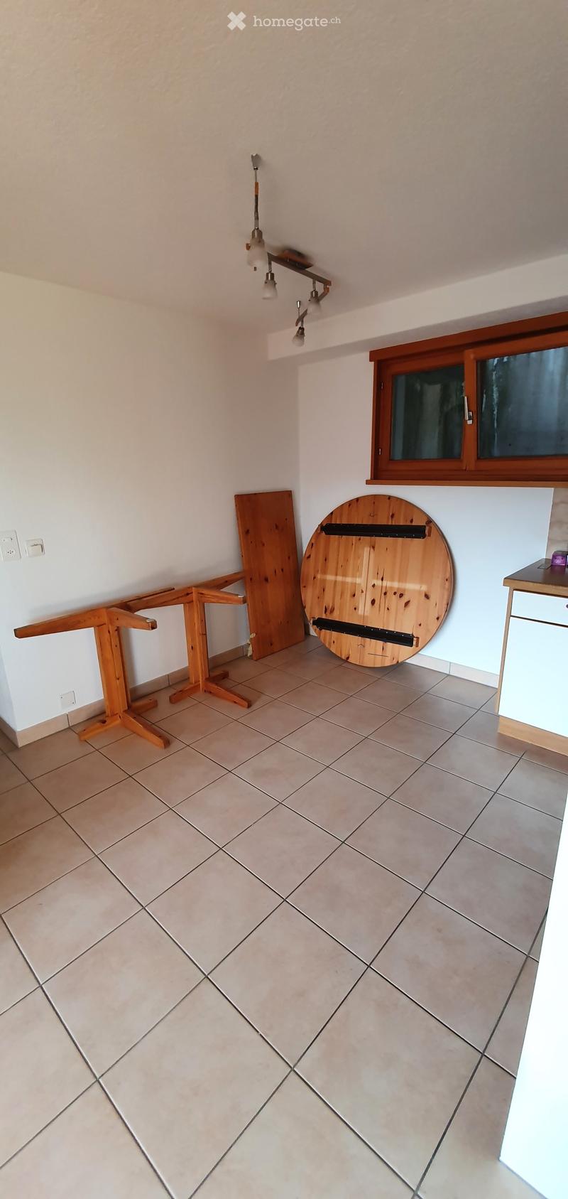 Empty room with tiled floor, white walls, and a window with wooden frame. There are some wooden items leaning against the wall, but no furniture or equipment.