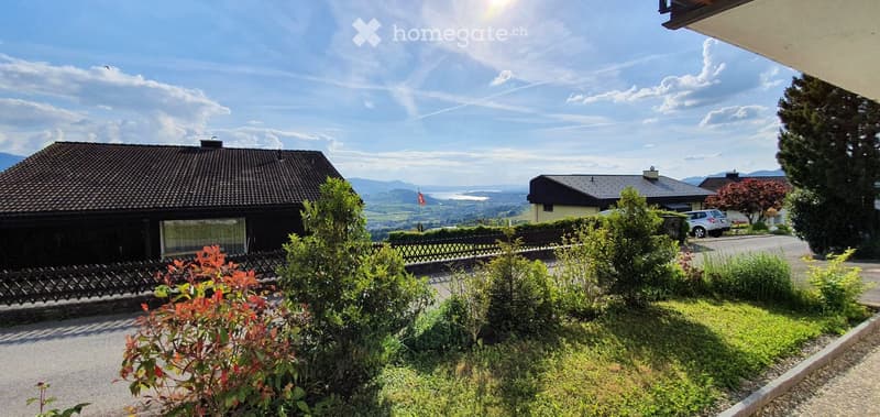 Two-story house with dark roof and large windows, surrounded by greenery and offering a scenic mountain view.