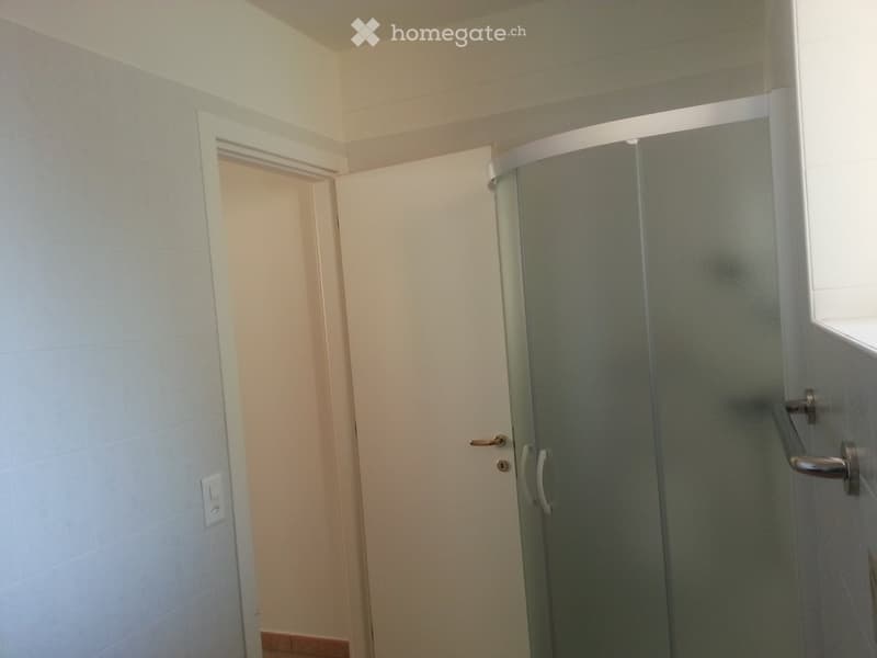 Bathroom with white tiled walls, entrance door, glass shower enclosure with chrome handles