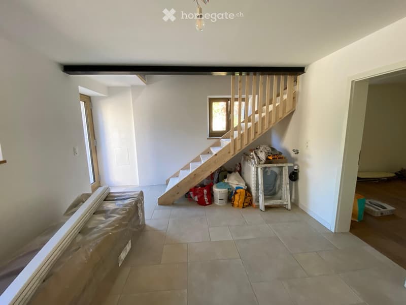Empty hallway with tiled floor, wooden staircase, and scattered construction materials and tools.
