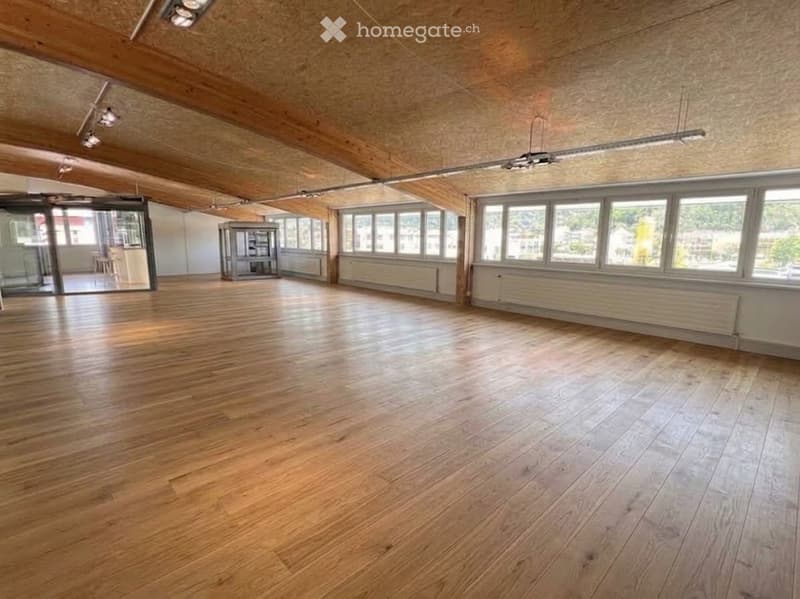 Empty room with wooden flooring, large windows, and exposed wooden beams on the ceiling. No furniture or equipment present.