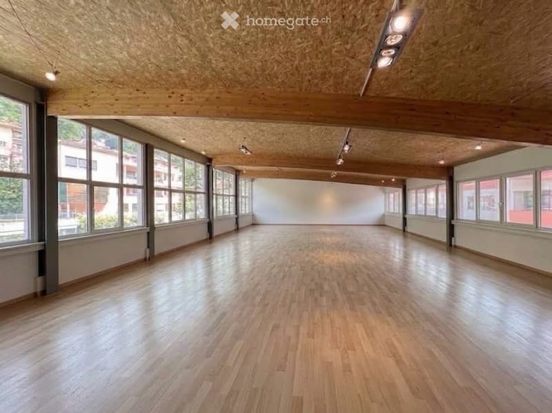 Empty room with wooden flooring, large windows, and exposed wooden ceiling beams.