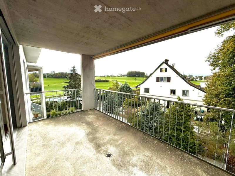 Balcony with metal railing, concrete floor, and scenic view of a green field and house.