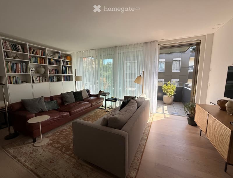 Modern living room with two sofas, a coffee table, a bookshelf, and a view to a balcony.