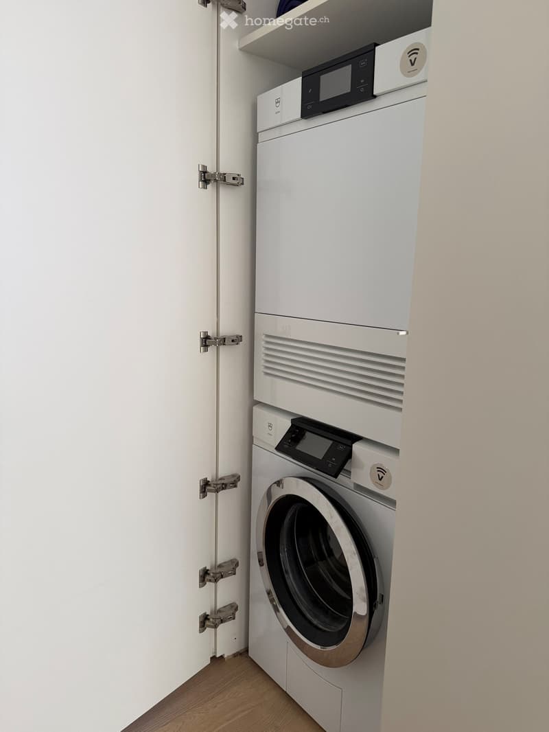 Modern, compact bathroom with a white washing machine and a dishwasher stacked vertically, featuring a sleek design and a wooden floor.