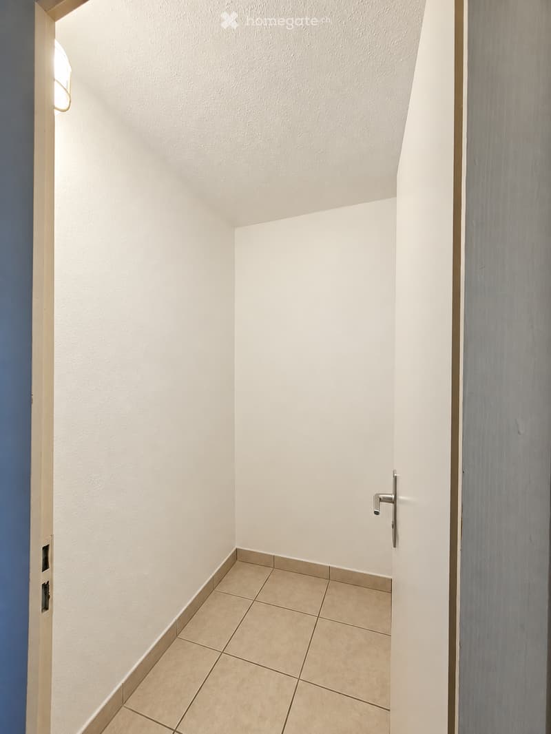 Empty hallway with white walls, tiled floor, and a closed door on the right side.