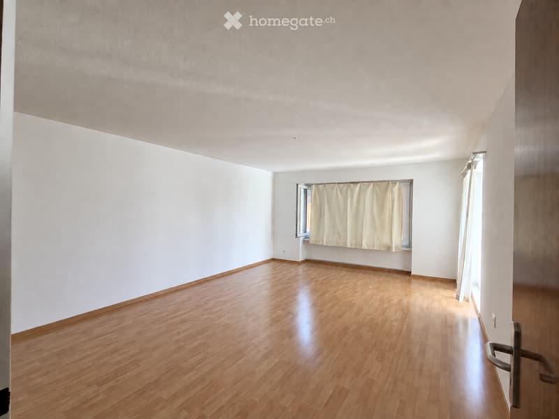 Empty room with wooden flooring, white walls, and a window with curtains.