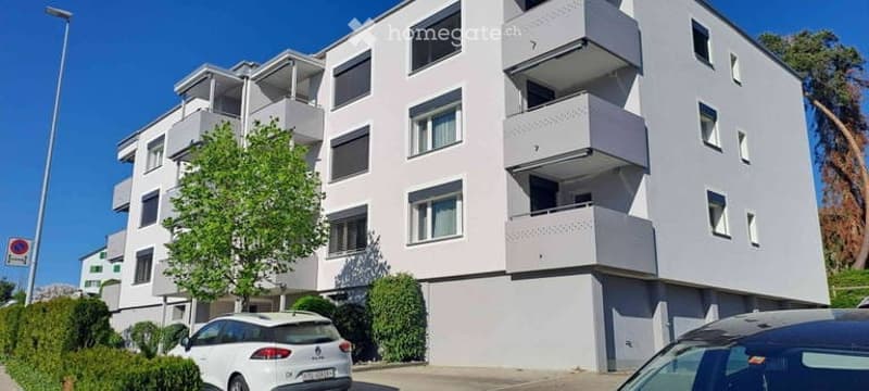 Modern multi-story apartment building with balconies, white exterior, and several windows.