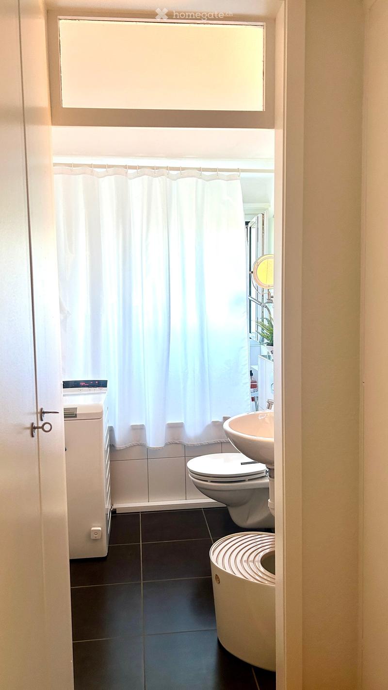 Modern bathroom with dark tiled floor, white toilet, sink, bathtub, and shower curtain. Features a large window above the shower area.