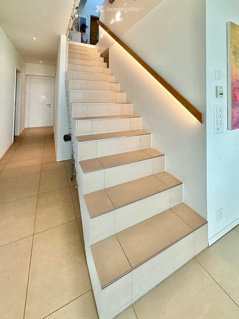 Modern staircase with beige tiles, wooden handrail, and integrated lighting, leading to an upper level.